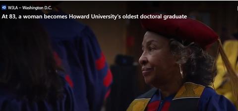 Woman with gray hair wearing graduation cap and gown at ceremony.